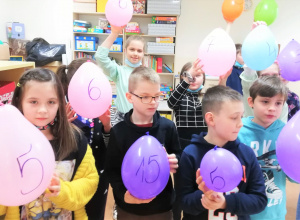 Dwoje dzieci trzyma w rękach kolorowe balony z namalowanymi na nich liczbami.